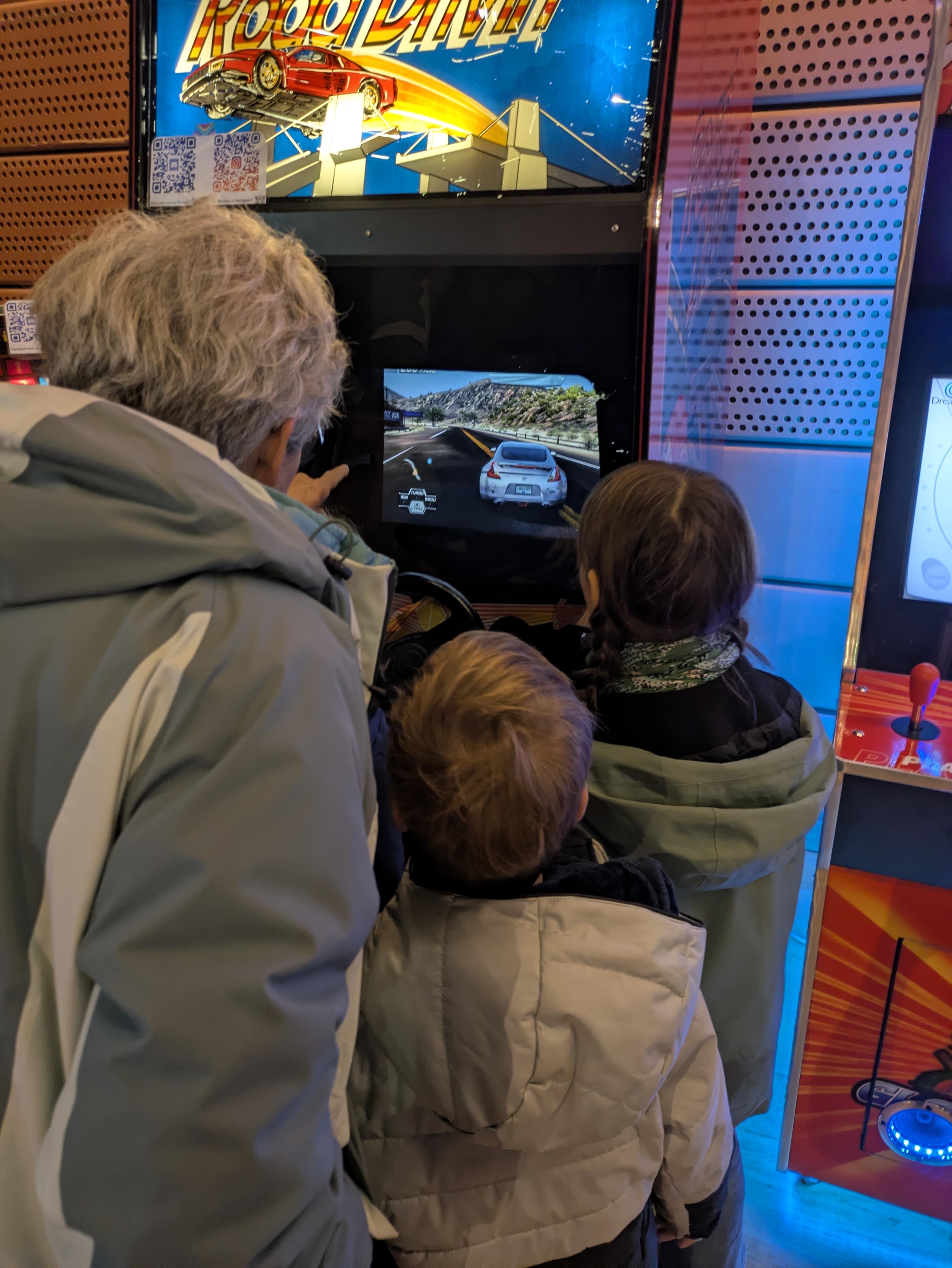 Une famille regardant un enfant jouer à Need For Speed sur la borne Road Drivin'